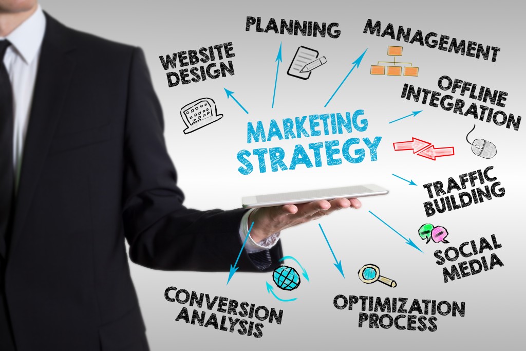 businessman holding a tablet surrounded by digital illustrations of marketing strategies