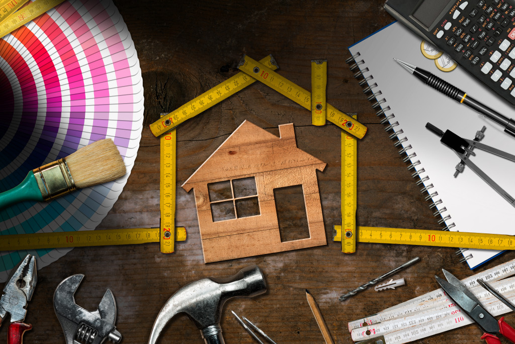 wooden home in the middle of tools and ruler sticks with calculator and color palettes on the side